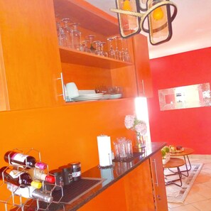 Una cocina con armarios color naranja, una estantería para vinos y un comedor con mesa y sillas.