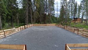 Un'area esterna recintata con fondo in ghiaia, circondata da alberi alti.