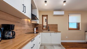 Een moderne keuken met houten aanrechtbladen, witte kastjes, een koffiezetapparaat en een raam met uitzicht.
