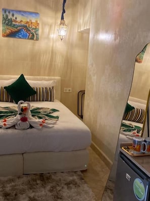 A hotel room with a bed, a mirror, a small refrigerator, and a painting on the wall. - Riad mon pote Marrakech (Marrakesh)