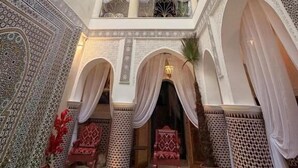 Vue intérieure d’un riad marocain traditionnel, caractérisé par ses décorations de carreaux complexes, ses arches et son plafond haut.