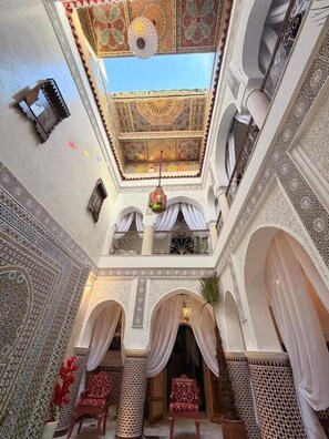 An interior view of a traditional Moroccan riad with ornate tile work, arches, and a high ceiling. - Riad mon pote Marrakech (Marrakesh)