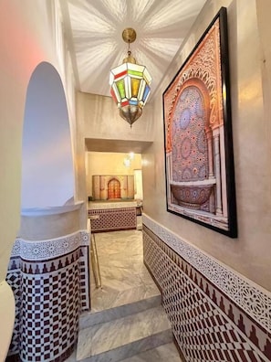 A hallway with ornate wall decorations, a patterned floor, and a hanging light fixture. - Riad mon pote Marrakech (Marrakesh)