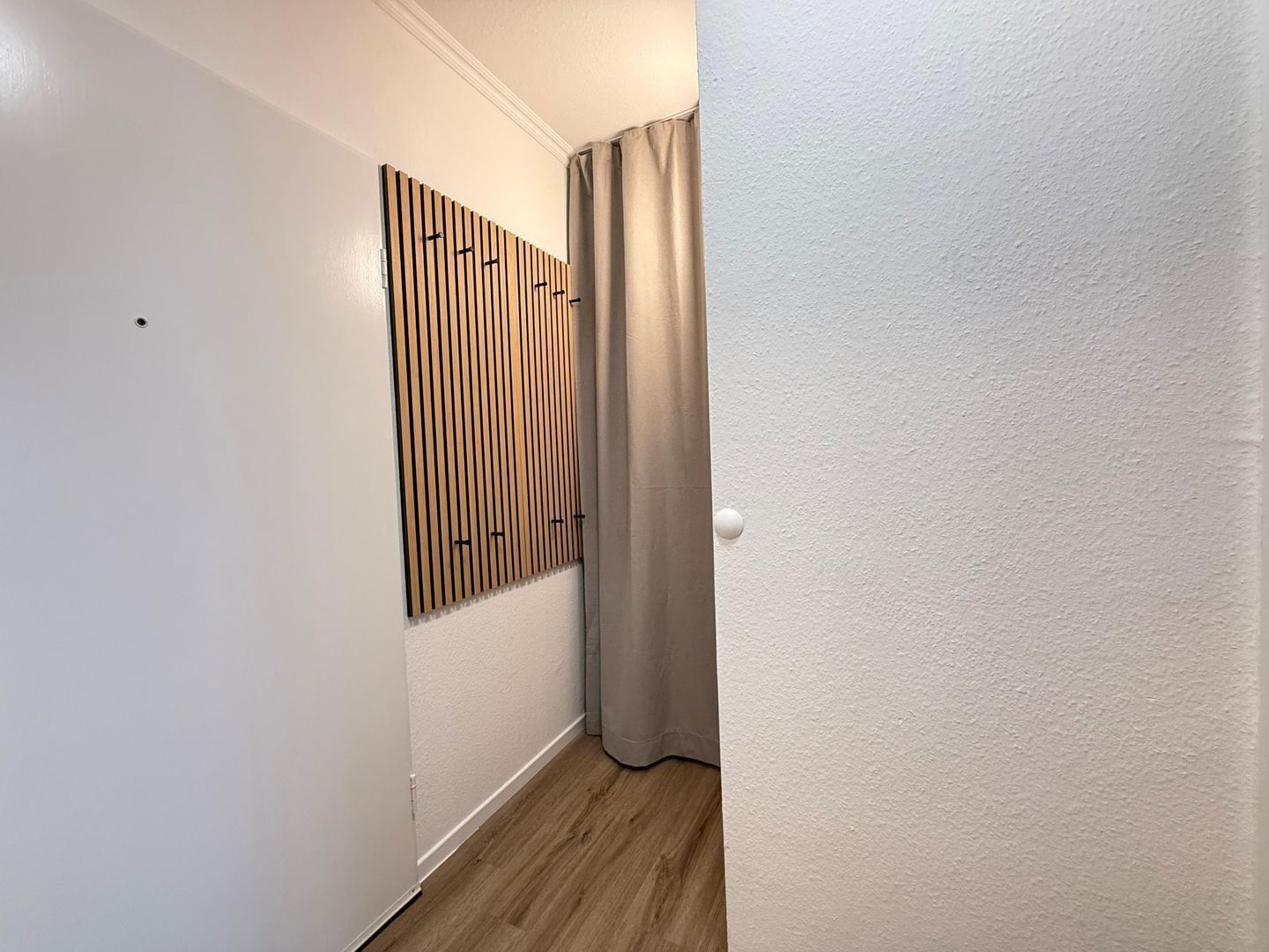 Un couloir étroit avec un mur lambrissé en bois, une porte dotée d’une poignée ronde et un rideau.
