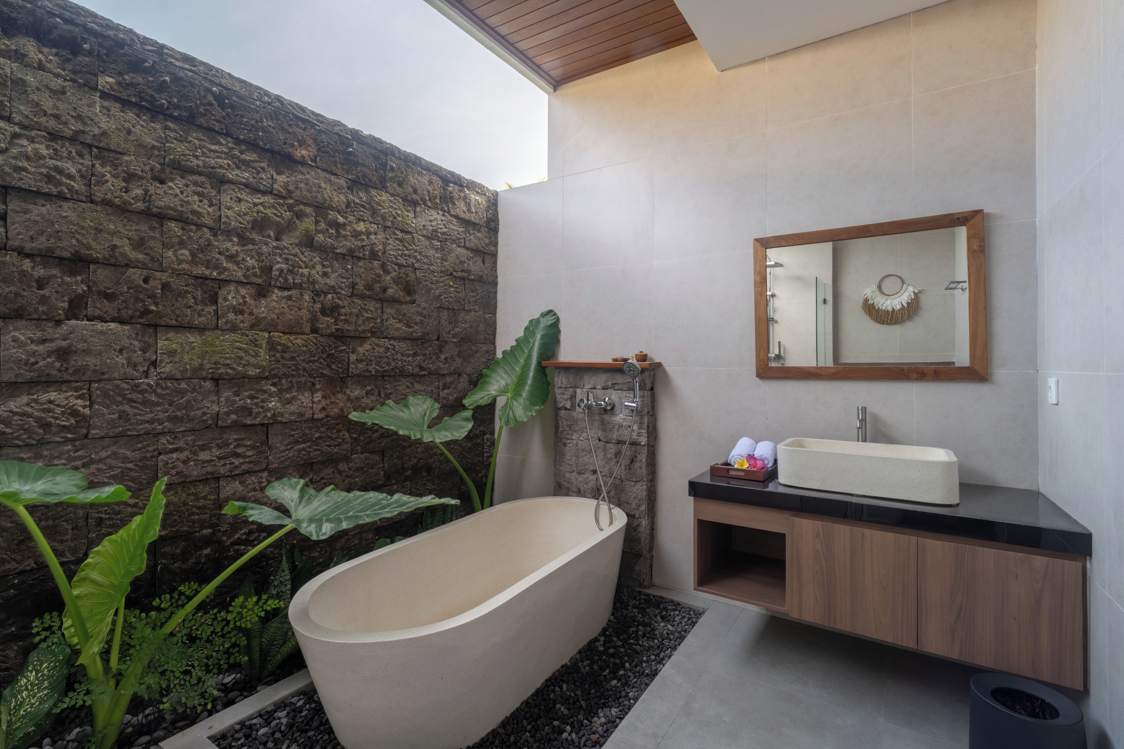 Un baño moderno con una bañera independiente, un tocador de madera, un espejo grande y una pared de piedra.