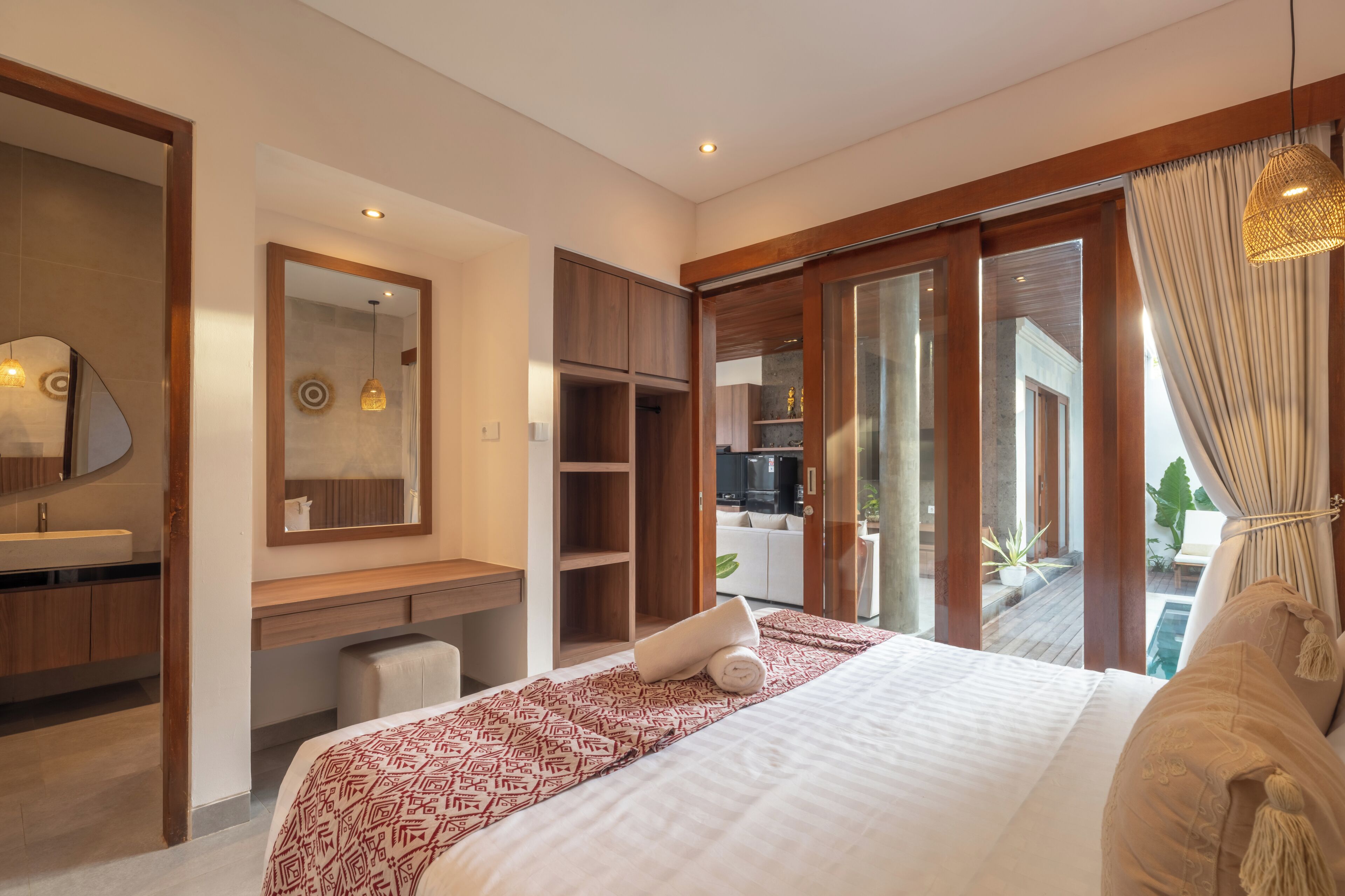 Quarto de hotel moderno com uma cama grande, escrivaninha embutida, toucador com espelho e porta de vidro deslizante para uma varanda.