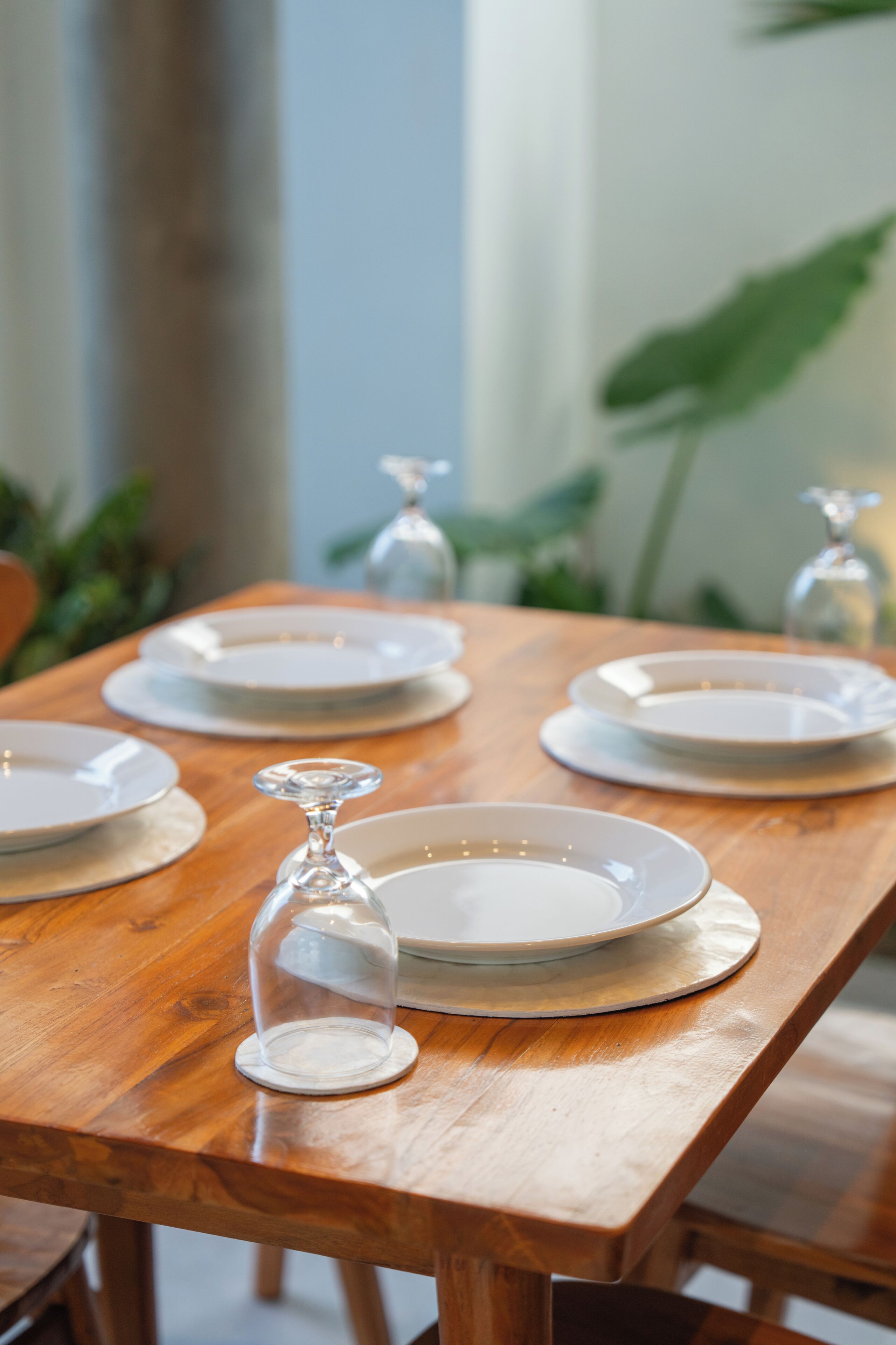 Una mesa de comedor de madera con platos blancos y una claraboya de vidrio como centro de mesa.
