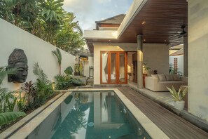 Un área de piscina moderna al aire libre, con una piscina cristalina rodeada de exuberante follaje y una terraza de madera.