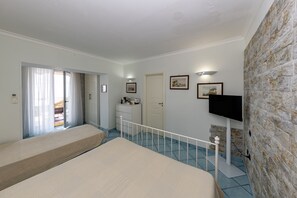 Ein Schlafzimmer mit zwei Betten, einem Fernseher, einer Steinwand und einer Tür, die auf einen Balkon führt.