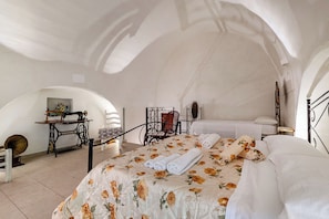 A bedroom with a floral bedspread, a sewing machine, a chair, and a bed with white linens. - Le Mesolecchie (Crispiano)