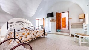 Ein Schlafzimmer mit gewölbter Decke, einem Bett mit floralem Überwurf, einer Holztür, einer weißen Kommode und einem Fernseher, der über der Tür angebracht ist.