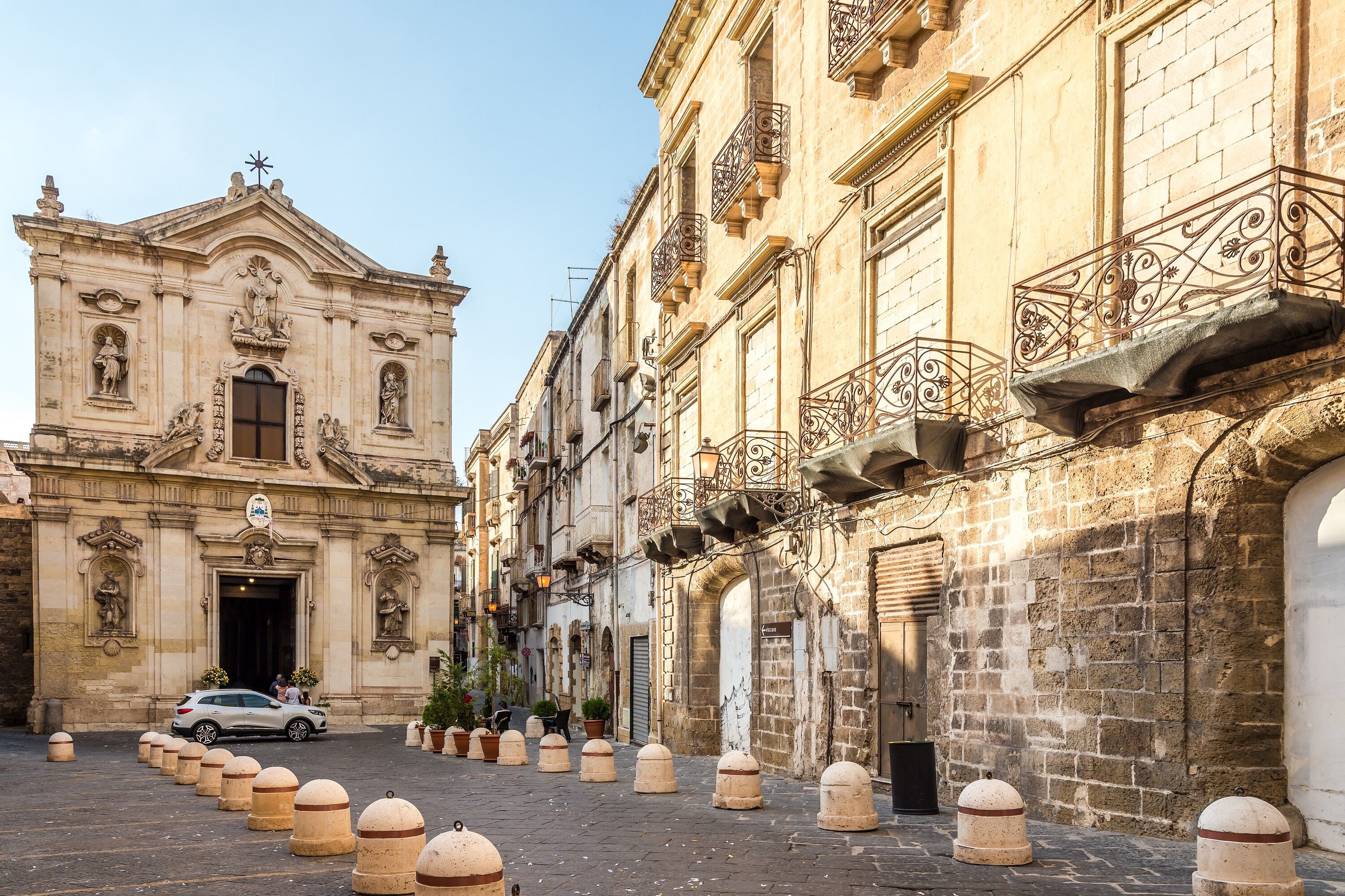 A historic building with ornate architectural details, a paved street, and bollards lining the sidewalk.