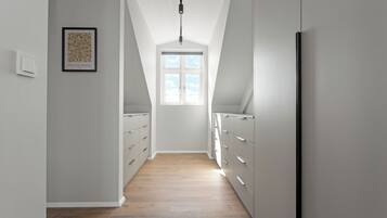 A narrow hallway with wooden flooring, white walls, and a window at the end.
