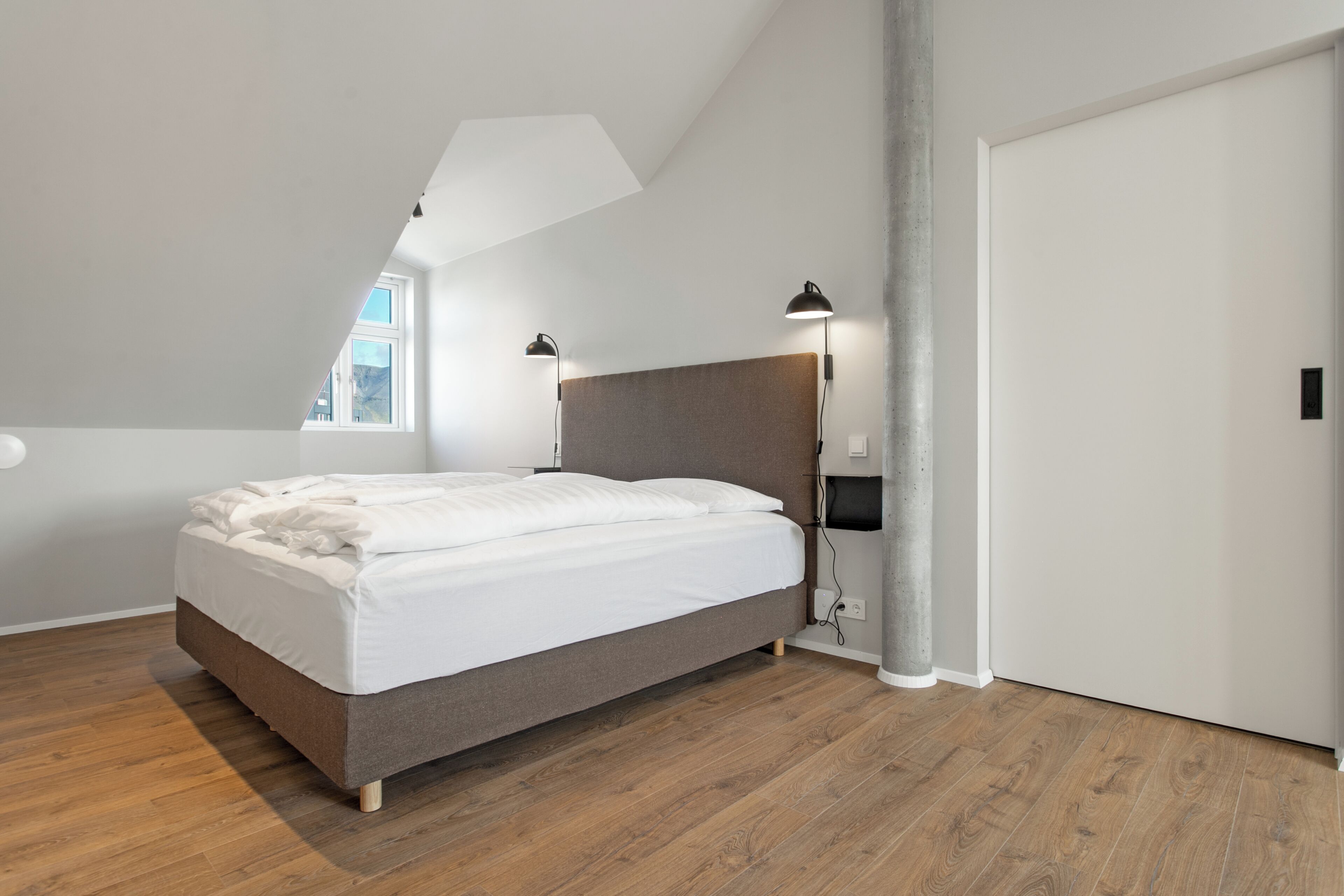 A bedroom with a bed, a window, a ceiling light, and a door.