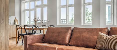 A modern living room with a brown leather sofa, a round coffee table, and a dining area with chairs and a table.