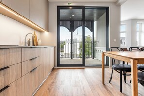 A modern kitchen with a wooden countertop, a dining table with chairs, and a sliding glass door leading to a balcony.