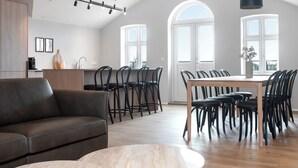 A modern living room with a sofa, dining table, chairs, and a kitchen area with a coffee machine.