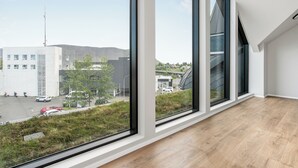 A room with large windows, a wooden floor, and a view of a building with a modern design.