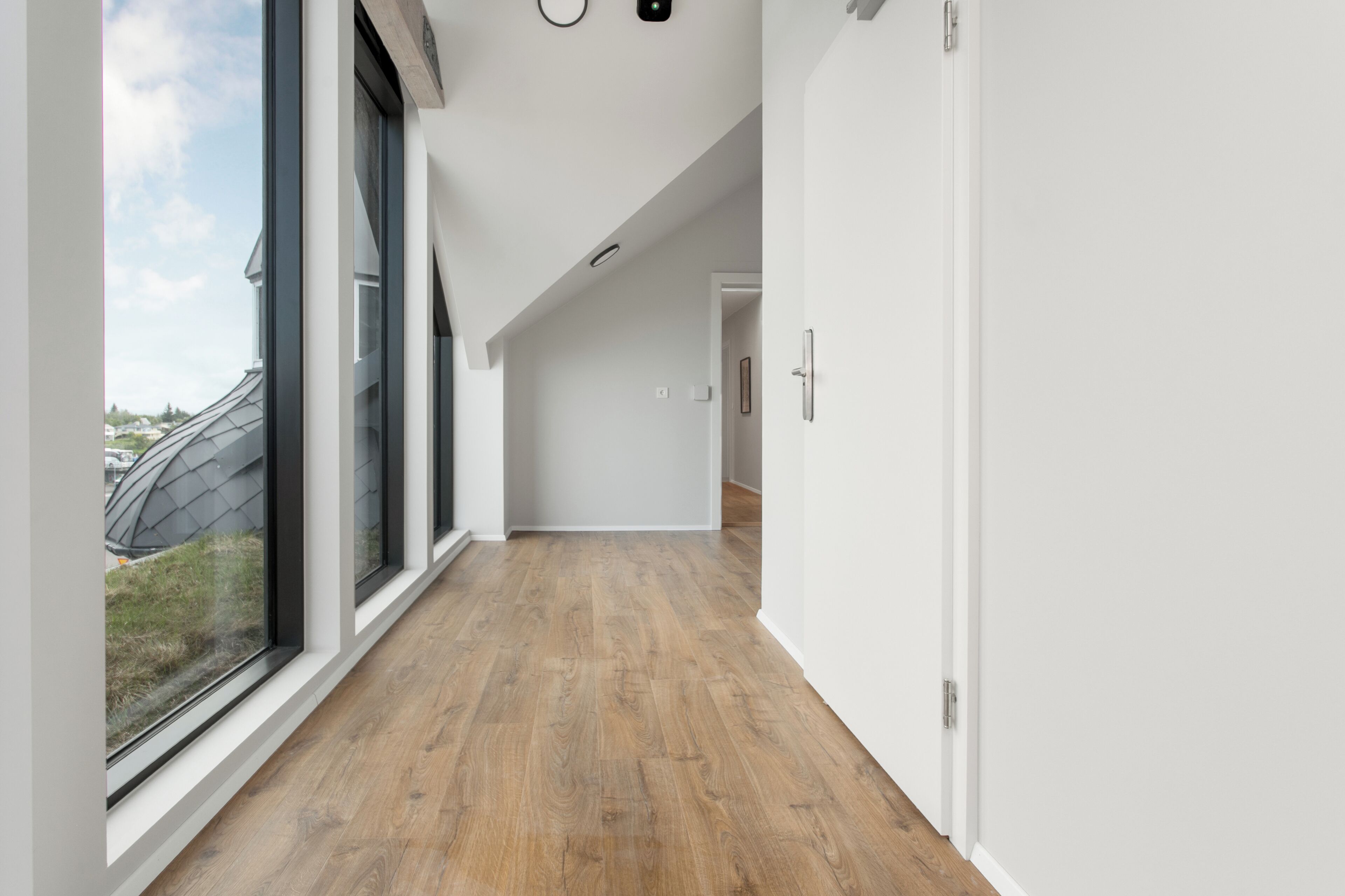 A modern hallway with large windows, wooden flooring, and white walls.