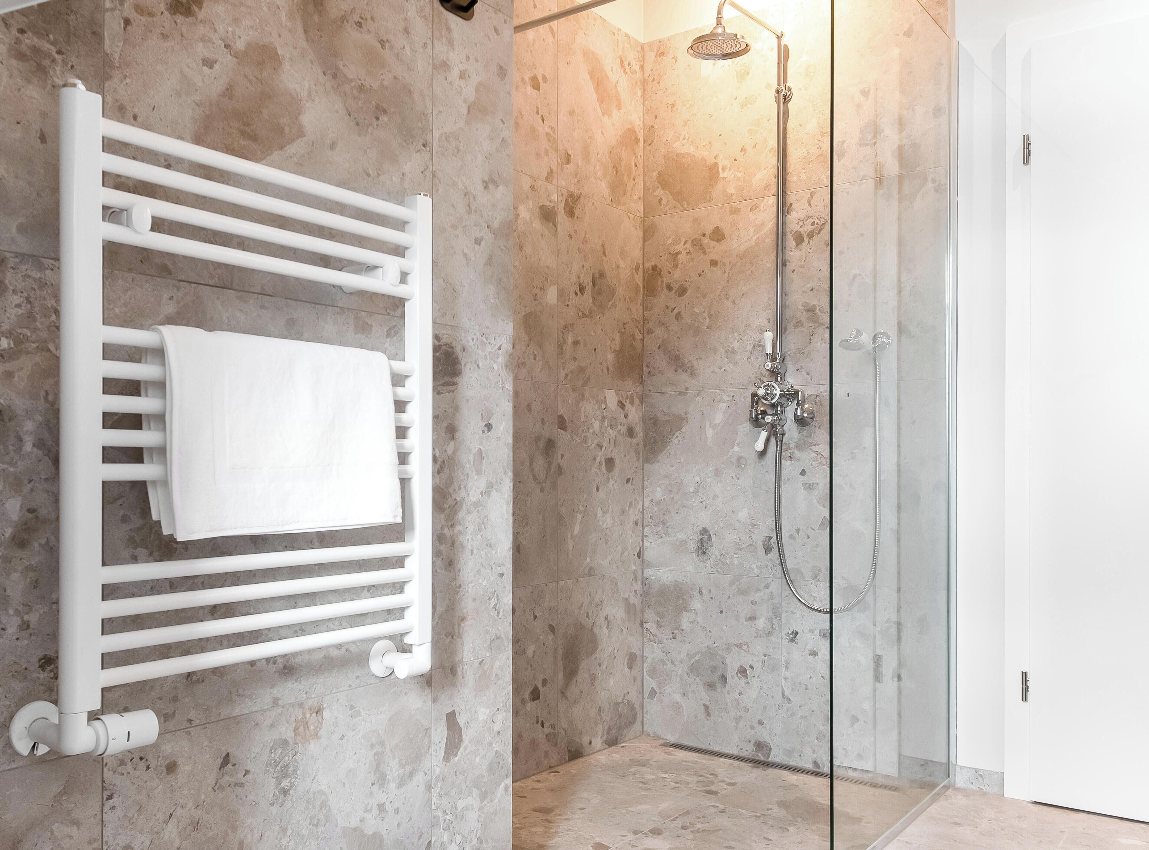 A bathroom with a white towel rack, a shower with a handheld showerhead, and a glass-enclosed shower stall.