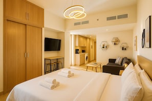 A hotel room with a large bed, a TV, a small kitchen area, and a seating area with a sofa. - Pure Voyage Azizi Riviera (Dubai)