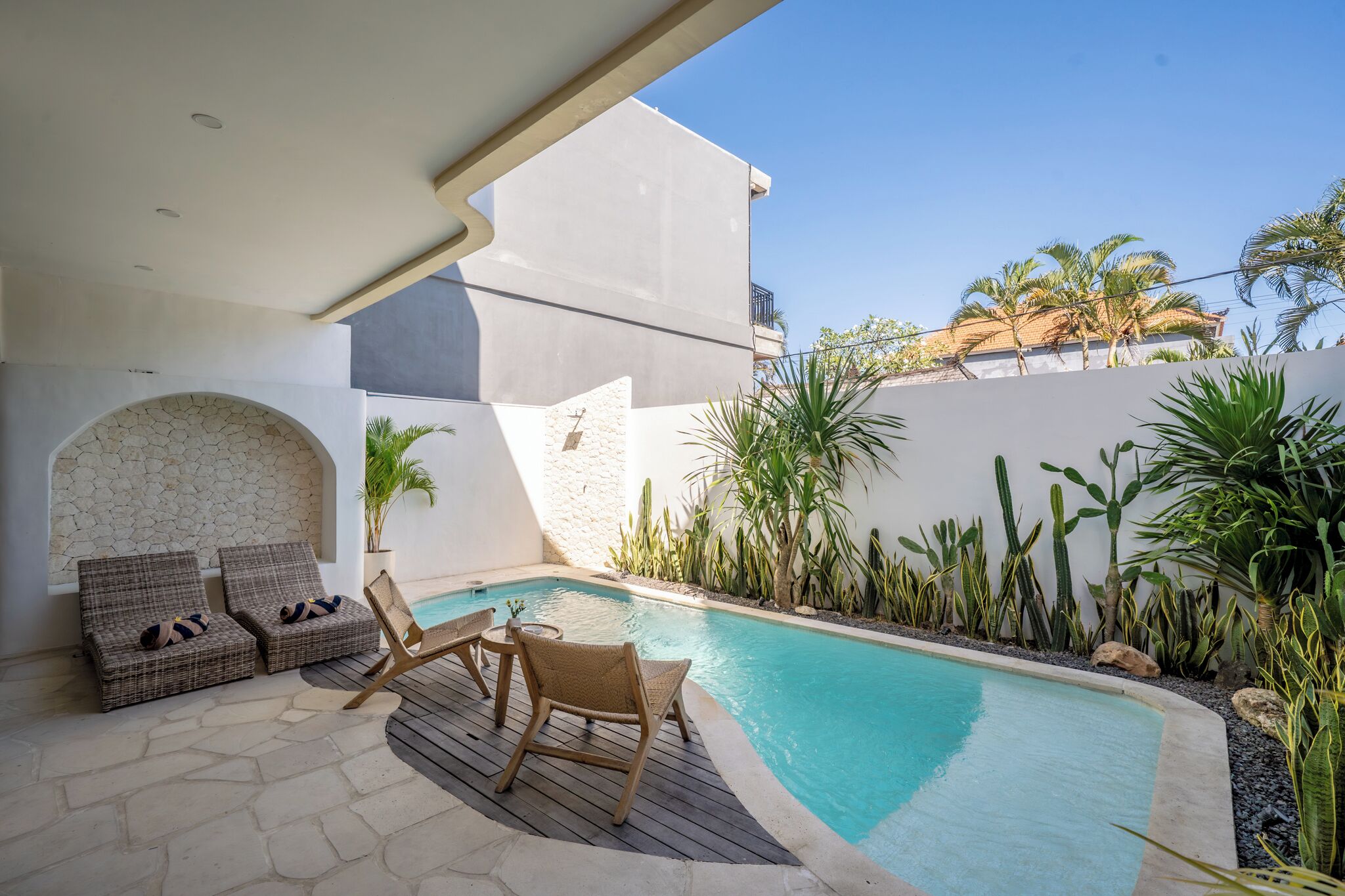 A pool area with lounge chairs, a small table, and a stone wall.