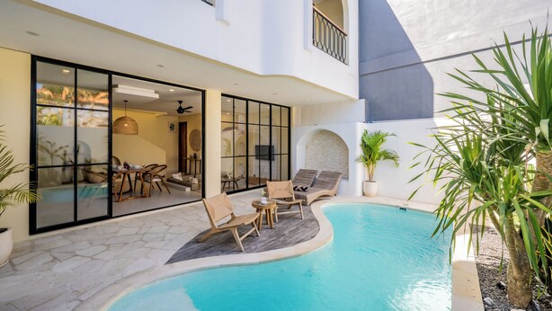Ein moderner Poolbereich mit Liegestühlen, einem Esstisch und einem mit Glas geschlossenen Raum mit Aussicht.