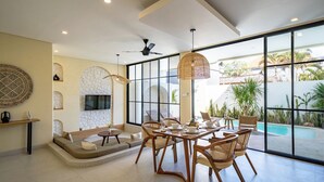 Ein modernes Interieur mit Essbereich, einem an einer Steinwand befestigten Fernseher und Blick auf einen Swimmingpool.