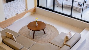 Ein modernes Wohnzimmer mit einem beigefarbenen Ecksofa, einem runden Couchtisch aus Holz und einem großen Fenster mit Blick auf Gartenmöbel.