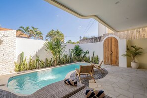 A pool area with lounge chairs, a wooden door, and various plants. - Villa Avalon Canggu (Canggu)