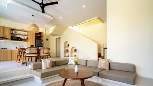 Ein modernes Wohnzimmer mit einer Couch, Sesseln, einem Couchtisch und einer Küchenzeile mit Schränken und Geräten.