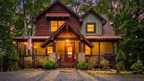 A two-story log cabin with a front porch, stone foundation, and an American flag. - Mt View, Spa, Firepit, EV Chrgr & Pvt Riverside Pk (Blue Ridge)