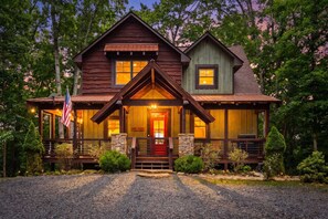 A two-story log cabin with a front porch, stone foundation, and an American flag. - Mt View, Spa, Firepit, EV Chrgr & Pvt Riverside Pk (Blue Ridge)