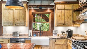 A rustic kitchen with wooden cabinets, a built-in oven, a coffee maker, and a window with a view of greenery. - Mt View, Spa, Firepit, EV Chrgr & Pvt Riverside Pk (Blue Ridge)