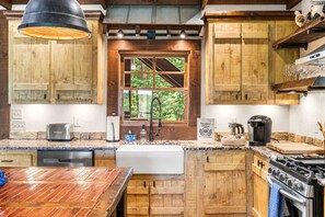 A rustic kitchen with wooden cabinets, a built-in oven, a coffee maker, and a window with a view of greenery. - Mt View, Spa, Firepit, EV Chrgr & Pvt Riverside Pk (Blue Ridge)