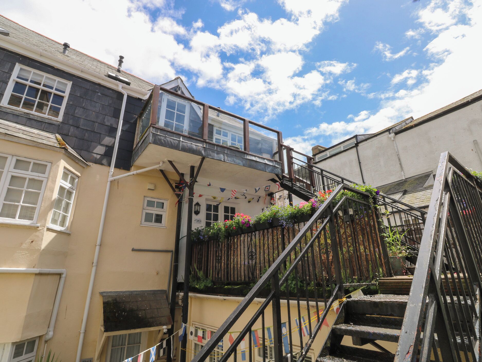 A multi-story building with a balcony, a staircase, and a small garden area.