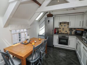 A kitchen with white cabinets, a stainless steel refrigerator, a wooden dining table with chairs, and a view of the outside through a window. - Top Storey (Dartmouth)