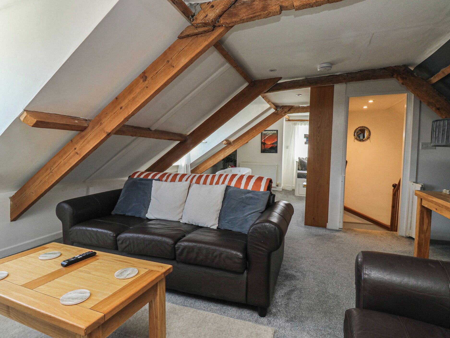 A loft-style room with exposed wooden beams, a leather sofa with striped pillows, a wooden coffee table, and a remote control.