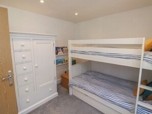A bunk bed with striped bedding, a white wardrobe with drawers, and a small shelf with books. - Top Storey (Dartmouth)