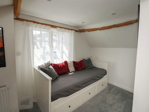 Ein Zimmer mit schrägem Dach, einem Bett mit Stauräumen, einem Fenster mit durchsichtigen Vorhängen und einer Heizung.