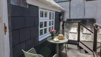 Ein kleiner Außenbereich mit Tisch und Stühlen, ein Fenster mit Ausblick und eine Treppe zu einer erhöhten Ebene.