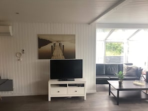 A living room with a flat-screen TV on a white cabinet, a sofa, a coffee table, and a large window. - 4 Star Holiday Home in Harboore (Harboore)
