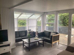 A covered patio area with a black leather sofa, a coffee table, and a television on a stand. - 4 Star Holiday Home in Harboore (Harboore)