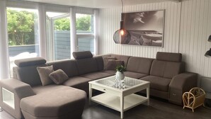 A modern living room with a sectional sofa, a glass coffee table, and a large window with a view of greenery. - 4 Star Holiday Home in Harboore (Harboore)