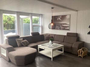 A modern living room with a sectional sofa, a glass coffee table, and a large window with a view of greenery. - 4 Star Holiday Home in Harboore (Harboore)