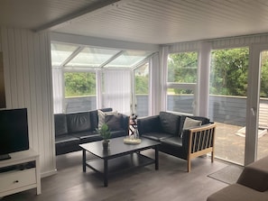 A covered patio with a black leather sofa, a coffee table, and a television on a stand. - 4 Star Holiday Home in Harboore (Harboore)