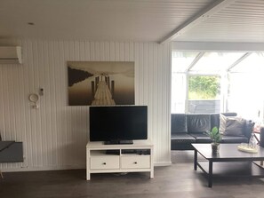 A living room with a flat-screen TV on a white cabinet, a black sofa, and a coffee table with a plant. - 4 Star Holiday Home in Harboore (Harboore)