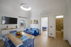 Ein modernes Wohnzimmer mit Esstisch, blauem Sofa und an der Wand montiertem Fernseher.
