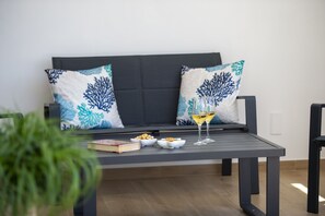 Ein moderner Außenbereich mit einer Couch, Kissen, einem Tisch und einem Glas Wein.