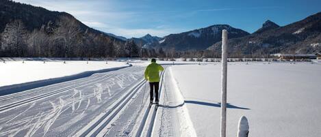 Una persona practica esquí de fondo sobre un sendero cubierto de nieve, con montañas al fondo.